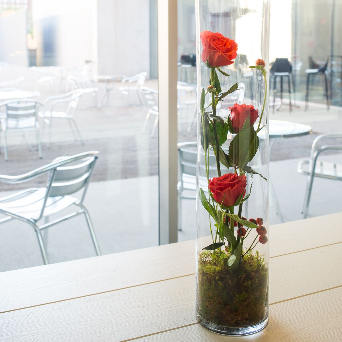 roses in a cylindrical glass vase on a table in a light, airy restaurant